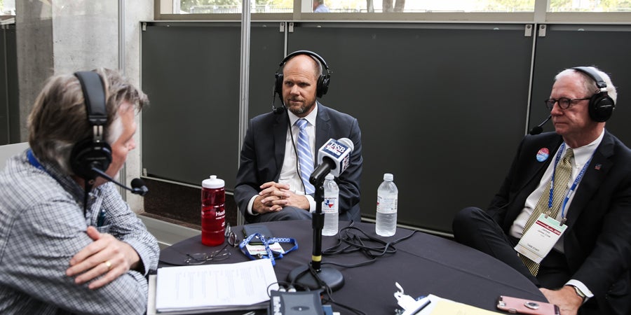 photo of 3 men with headphones sitting across each other, participating in a new podcast