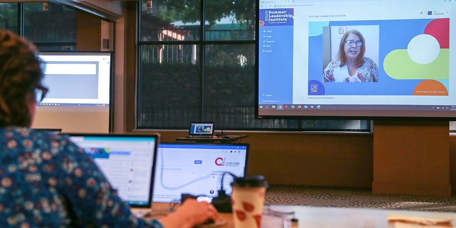 photo of a woman working on her laptop in a conference room with a projector screen displaying a virtual meeting
