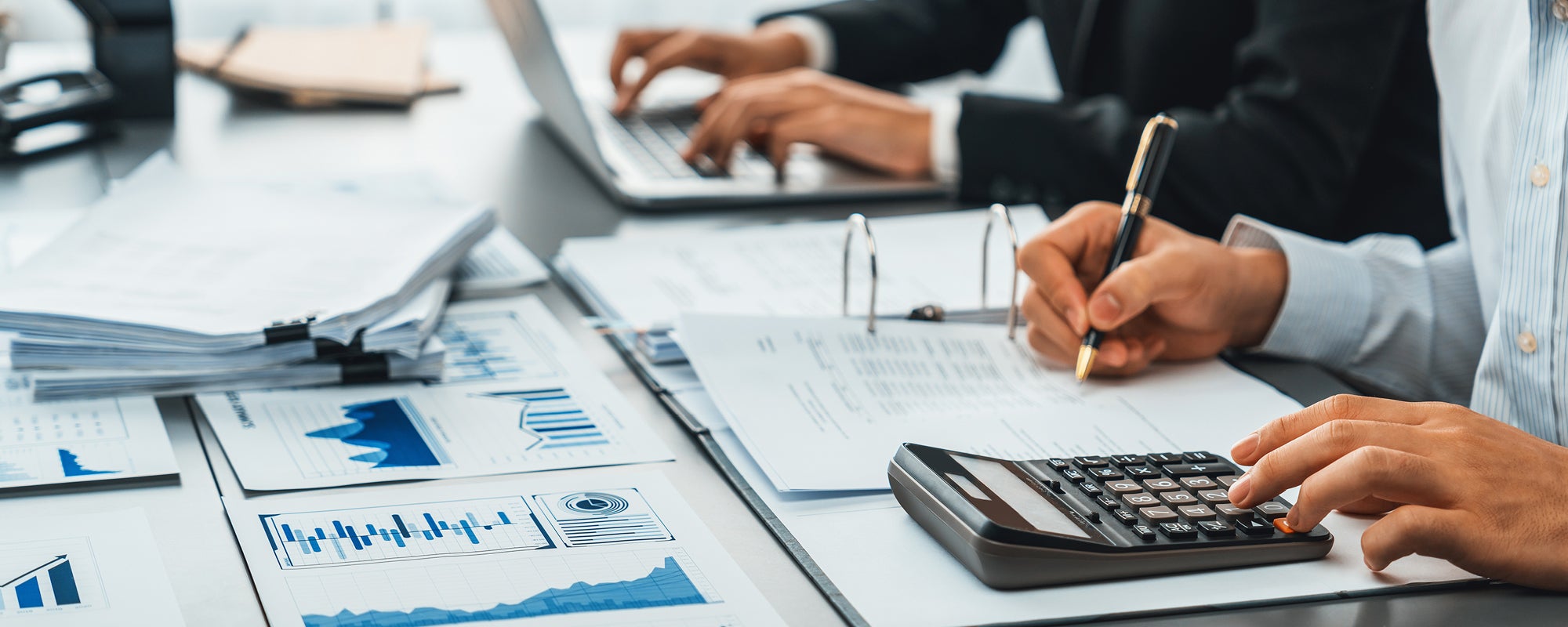 photo of a person working on a budget with left hand typing on a calculator and right hand holding a pen over a document